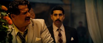 Movie still from “The Devil's Double” (2011), directed by Lee Tamahori – A man in a suit and tie standing next to another man in a suit and tie; Close Up shot, Over the shoulder angle