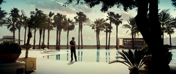 Movie still from “The Devil's Double” (2011), directed by Lee Tamahori – A man standing in front of a swimming pool with palm trees; Extreme Wide shot, Low angle