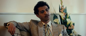 Movie still from “The Devil's Double” (2011), directed by Lee Tamahori – A man in a suit and tie sitting in a chair; Close Up shot, Low angle