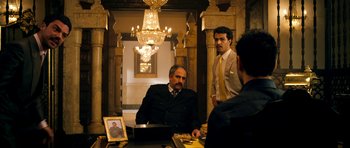 Movie still from “The Devil's Double” (2011), directed by Lee Tamahori – A man sitting at a table in front of two other men; Wide shot, Low angle