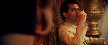 Movie still from “The Devil's Double” (2011), directed by Lee Tamahori – A man sitting in a chair in front of an ornate wall; Close Up shot, Over the shoulder angle