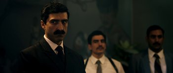 Movie still from “The Devil's Double” (2011), directed by Lee Tamahori – A man in a suit and tie standing next to another man in a tie; Close Up shot, Over the shoulder angle