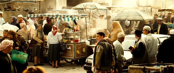 Movie still from “The Devil's Double” (2011), directed by Lee Tamahori – A group of people standing around a food stand; Wide shot, High angle
