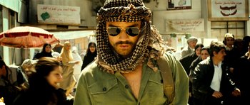 Movie still from “The Devil's Double” (2011), directed by Lee Tamahori – A man wearing a hat and sunglasses with a scarf around his neck; Close Up shot, Over the shoulder angle
