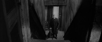Movie still from “The Diary of Anne Frank” (1959), directed by George Stevens – An old man in a coat and hat is standing in a door way; Wide shot, Low angle