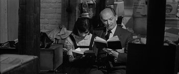 Movie still from “The Diary of Anne Frank” (1959), directed by George Stevens – A man and a woman sitting in a room reading books; Medium shot, High angle