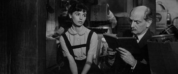 Movie still from “The Diary of Anne Frank” (1959), directed by George Stevens – A woman sitting in a chair holding a book; Medium shot, Over the shoulder angle