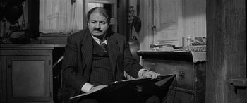 Movie still from “The Diary of Anne Frank” (1959), directed by George Stevens – A man in a suit sitting in front of an open book; Medium shot, High angle
