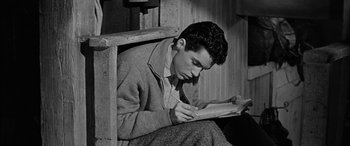 Movie still from “The Diary of Anne Frank” (1959), directed by George Stevens – A man sitting in a chair while reading a book; Medium shot, High angle