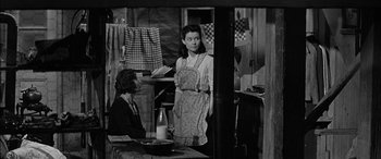 Movie still from “The Diary of Anne Frank” (1959), directed by George Stevens – A woman standing next to another woman in a kitchen; Medium shot, Over the shoulder angle