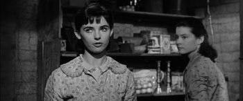 Movie still from “The Diary of Anne Frank” (1959), directed by George Stevens – A black - and - white photo of a woman standing in front of shelves; Close Up shot, Over the shoulder angle