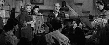 Movie still from “The Diary of Anne Frank” (1959), directed by George Stevens – A group of men and women sitting in a living room; Medium shot, Over the shoulder angle
