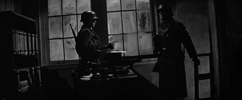 Movie still from “The Diary of Anne Frank” (1959), directed by George Stevens – Two men in uniforms are standing in front of a window; Medium shot, Low angle