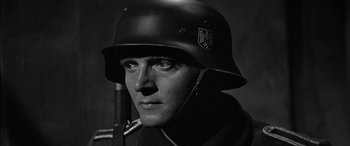 Movie still from “The Diary of Anne Frank” (1959), directed by George Stevens – A man wearing a german helmet with a rifle in the background; Close Up shot, Over the shoulder angle