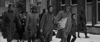 Movie still from “The Diary of Anne Frank” (1959), directed by George Stevens – A group of people walking down a street carrying luggage; Medium shot, Low angle