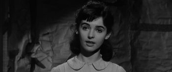 Movie still from “The Diary of Anne Frank” (1959), directed by George Stevens – A young woman in a white shirt is standing in front of a rock wall; Close Up shot, High angle