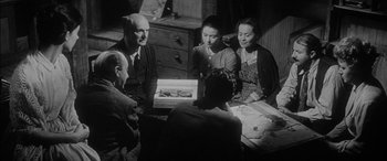 Movie still from “The Diary of Anne Frank” (1959), directed by George Stevens – A group of people sitting around a table talking; Medium shot, High angle