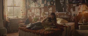 Movie still from “The Diary of a Teenage Girl” (2015), directed by Marielle Heller – A woman sitting on a bed in a room with pictures on the wall; Wide shot, High angle