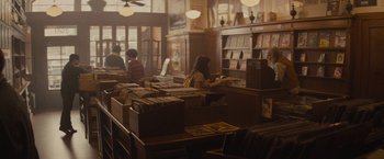 Movie still from “The Diary of a Teenage Girl” (2015), directed by Marielle Heller – A woman sitting at a table in a room filled with books; Wide shot, High angle