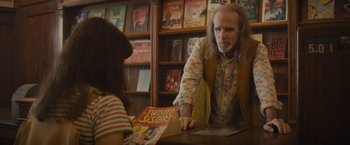 Movie still from “The Diary of a Teenage Girl” (2015), directed by Marielle Heller – A man is handing a book to a woman; Medium shot, Over the shoulder angle