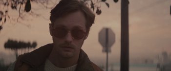 Movie still from “The Diary of a Teenage Girl” (2015), directed by Marielle Heller – A person wearing sunglasses near a street sign; Close Up shot, Low angle