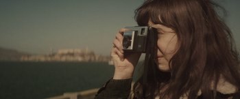 Movie still from “The Diary of a Teenage Girl” (2015), directed by Marielle Heller – A woman taking a picture with a camera; Close Up shot, High angle