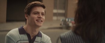Movie still from “The Diary of a Teenage Girl” (2015), directed by Marielle Heller – A young man smiling while sitting next to another man; Close Up shot, Over the shoulder angle