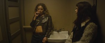 Movie still from “The Diary of a Teenage Girl” (2015), directed by Marielle Heller – A woman smoking a cigarette in front of a bathroom sink; Medium shot, Over the shoulder angle