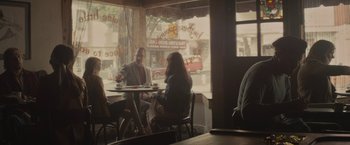 Movie still from “The Diary of a Teenage Girl” (2015), directed by Marielle Heller – A man and woman sitting at a table in front of a store window; Wide shot, Over the shoulder angle