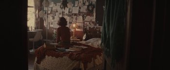 Movie still from “The Diary of a Teenage Girl” (2015), directed by Marielle Heller – A woman sitting on a bed in front of a wall of pictures; Wide shot, Over the shoulder angle