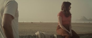 Movie still from “The Diary of a Teenage Girl” (2015), directed by Marielle Heller – A woman sitting on a wall looking out at the beach; Medium shot, High angle