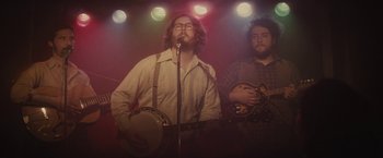 Movie still from “The Diary of a Teenage Girl” (2015), directed by Marielle Heller – A man singing into a microphone while another man plays a guitar; Medium shot, Low angle