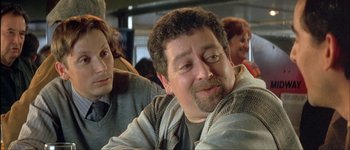 Movie still from “Le Dîner de Cons” (1998), directed by Francis Veber – A person sitting with another person; Close Up shot, Over the shoulder angle