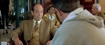 Movie still from “Le Dîner de Cons” (1998), directed by Francis Veber – A man in a suit sitting in front of a woman in a suit; Medium shot, Over the shoulder angle