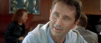 Movie still from “Le Dîner de Cons” (1998), directed by Francis Veber – A person with blue eyes smiling; Close Up shot, Low angle