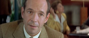 Movie still from “Le Dîner de Cons” (1998), directed by Francis Veber – A person wearing a suit and tie; Close Up shot, Over the shoulder angle