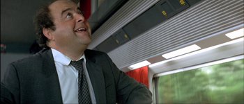Movie still from “Le Dîner de Cons” (1998), directed by Francis Veber – A man wearing a suit and tie on a train; Medium shot, Low angle