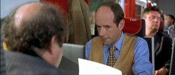 Movie still from “Le Dîner de Cons” (1998), directed by Francis Veber – A man in a vest and tie talking to another man in a suit; Close Up shot, Over the shoulder angle