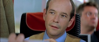 Movie still from “Le Dîner de Cons” (1998), directed by Francis Veber – A person sitting in a chair wearing a tie; Close Up shot, Over the shoulder angle