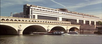 Movie still from “Le Dîner de Cons” (1998), directed by Francis Veber – A boat traveling on a river under a large bridge; Extreme Wide shot, High angle