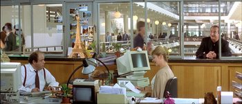 Movie still from “Le Dîner de Cons” (1998), directed by Francis Veber – A woman sitting at a computer desk in front of an eiffel tower; Wide shot, High angle