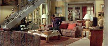 Movie still from “Le Dîner de Cons” (1998), directed by Francis Veber – A man sitting on top of a couch in a living room; Wide shot, High angle
