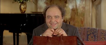 Movie still from “Le Dîner de Cons” (1998), directed by Francis Veber – A man in a suit and tie holding a brown bag; Close Up shot, High angle