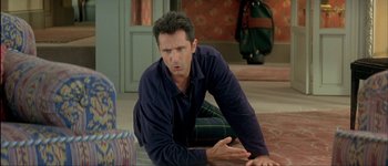 Movie still from “Le Dîner de Cons” (1998), directed by Francis Veber – A man sitting on the ground in a room; Medium shot, High angle