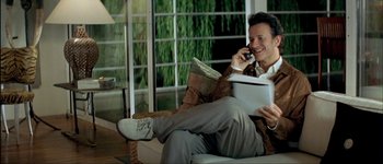 Movie still from “Le Dîner de Cons” (1998), directed by Francis Veber – A man sitting on a couch talking on a cell phone; Medium shot, High angle