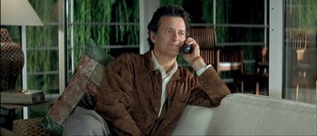 Movie still from “Le Dîner de Cons” (1998), directed by Francis Veber – A man sitting on a couch talking on a cell phone; Medium shot, High angle