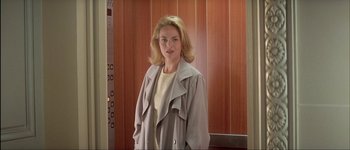 Movie still from “Le Dîner de Cons” (1998), directed by Francis Veber – A woman wearing a beige coat standing in front of a wooden wall; Medium shot, Low angle