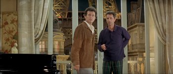 Movie still from “Le Dîner de Cons” (1998), directed by Francis Veber – A couple of men standing next to each other in a room; Medium shot, Low angle