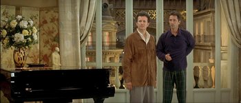 Movie still from “Le Dîner de Cons” (1998), directed by Francis Veber – Two men standing next to each other in front of a piano; Medium shot, Low angle