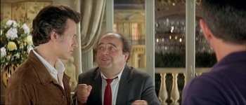Movie still from “Le Dîner de Cons” (1998), directed by Francis Veber – A man in a suit and red tie talking to another man in a suit and red tie; Medium shot, Over the shoulder angle